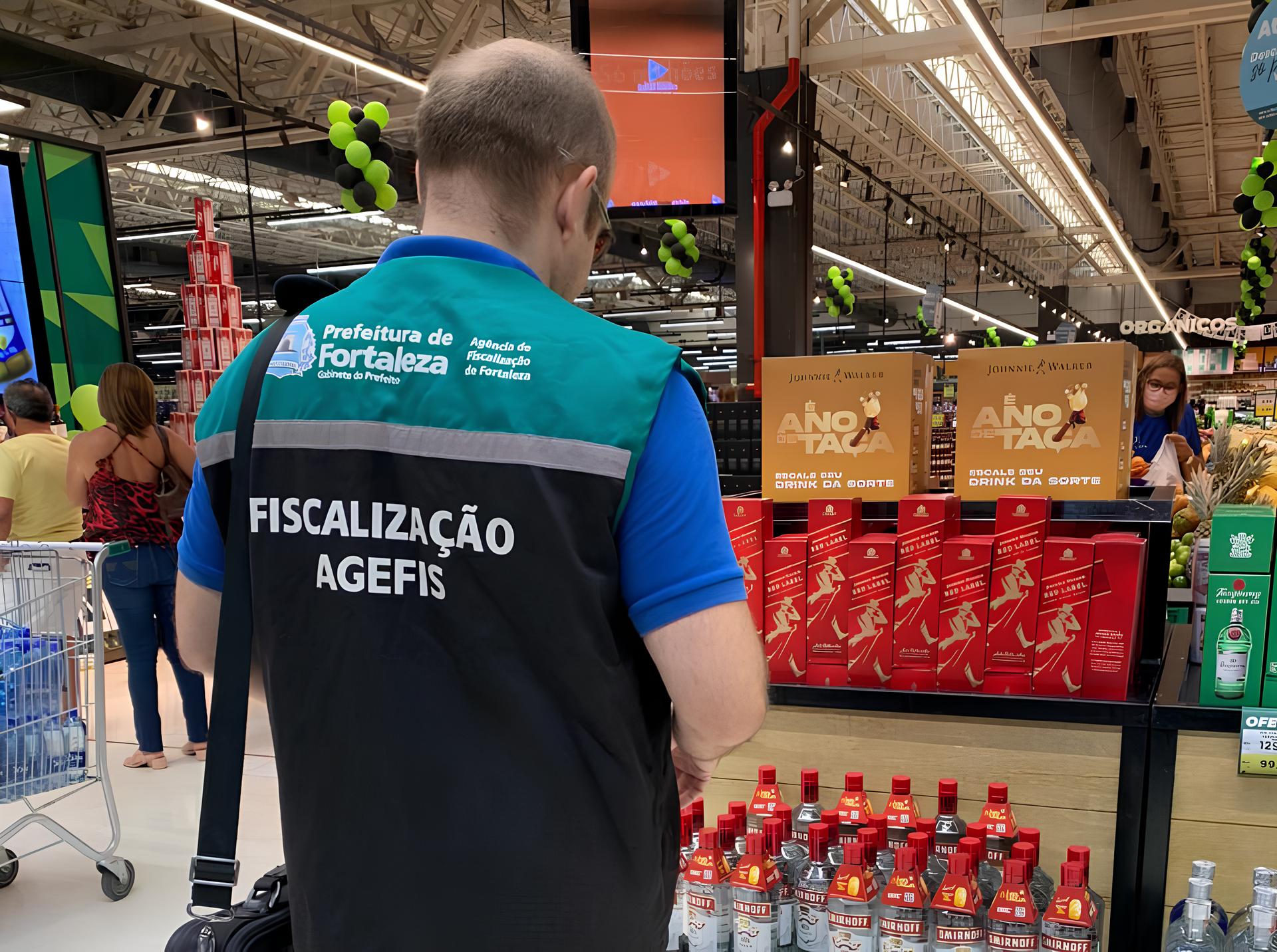 fiscal da agefis de costas na frente uma prateleira de bebidas alcoólicas